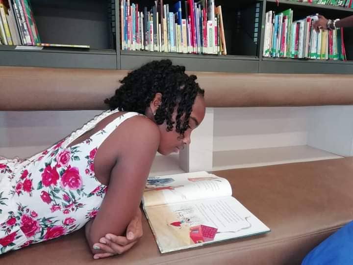 la imagen puecontener a una niña acostada en una banca,leyendo un libro 